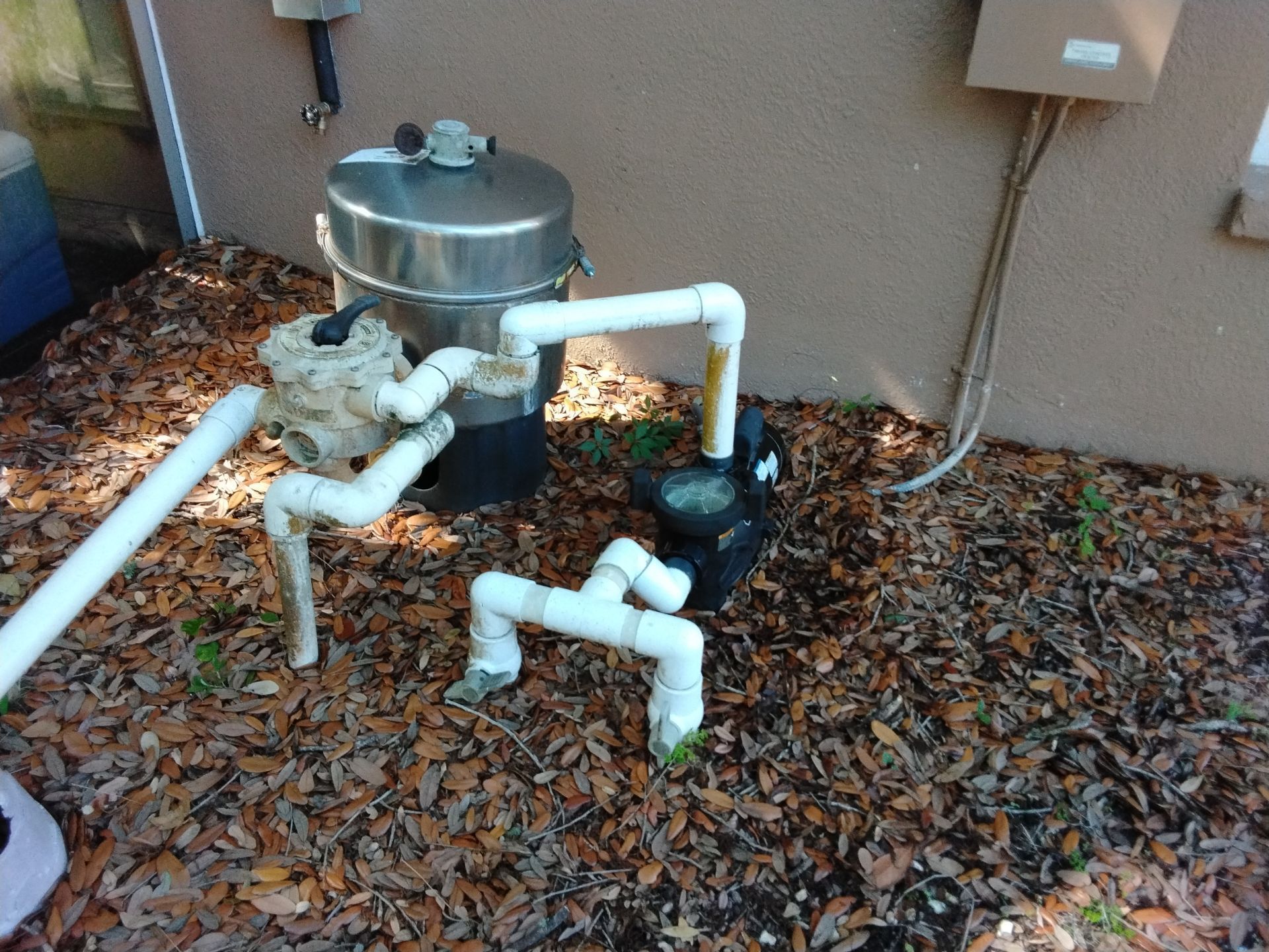 Outdoor utility pipes and a metal tank beside a house, covered in fallen leaves.