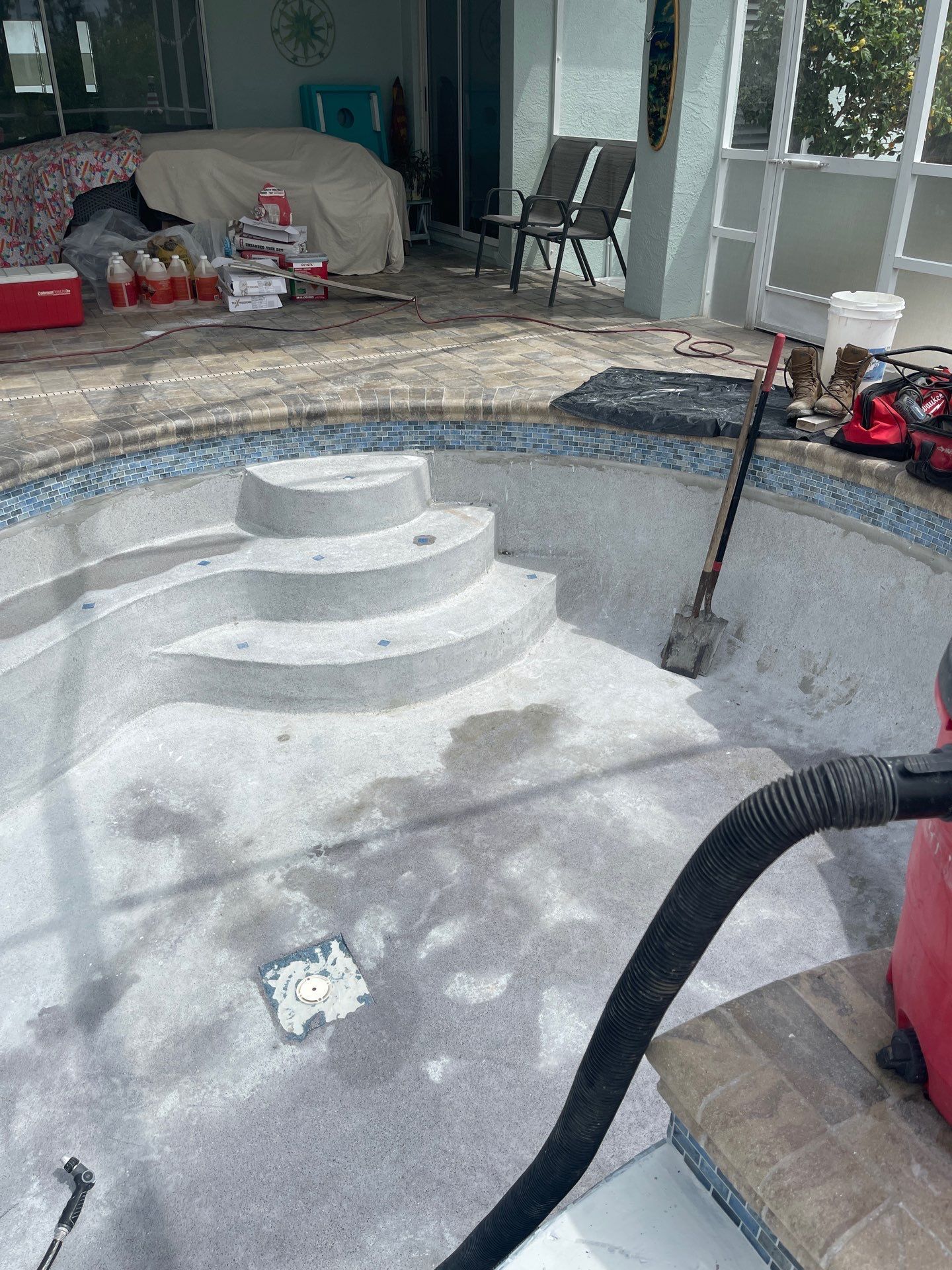 Empty pool under renovation with white step platform, tools, and hoses around the deck.