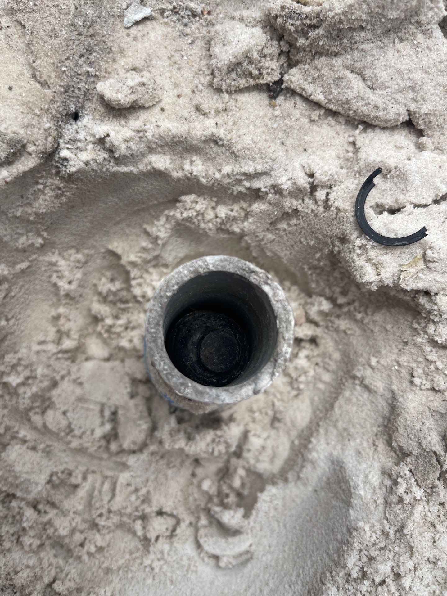 Round metal pipe opening in sandy ground with a small black cable loop nearby.