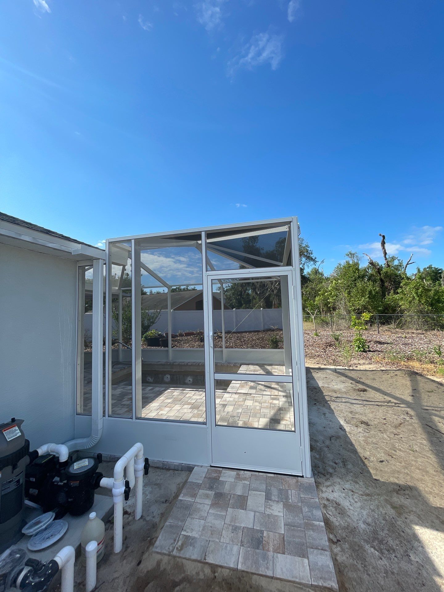 White porch enclosure frame beside a house, with tiled patio and blue sky in a yard.