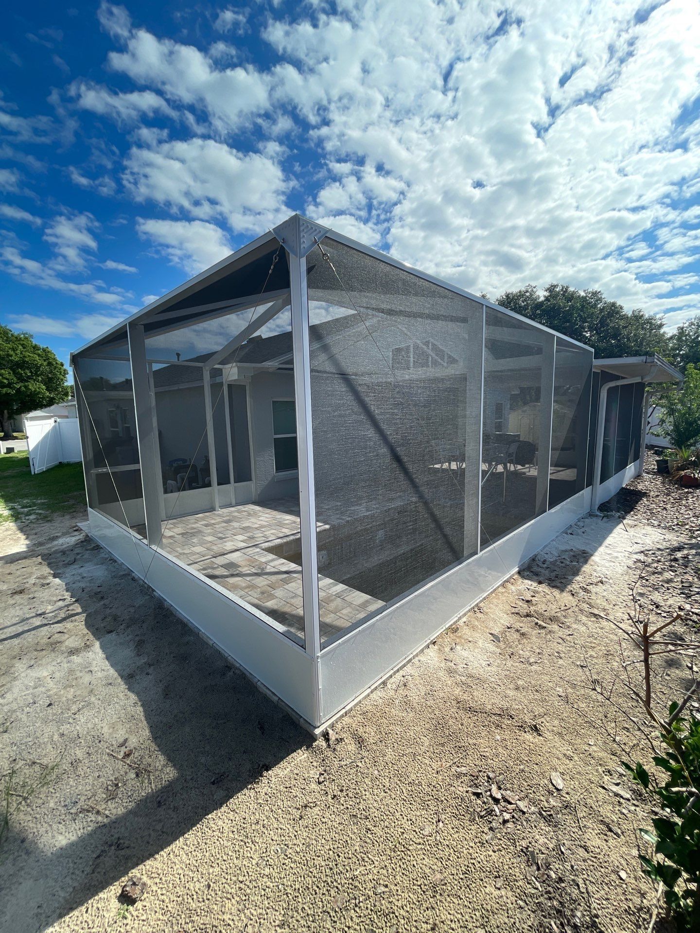 Screened porch under construction with gray framing and mesh walls on a gravel lot under a blue sky.