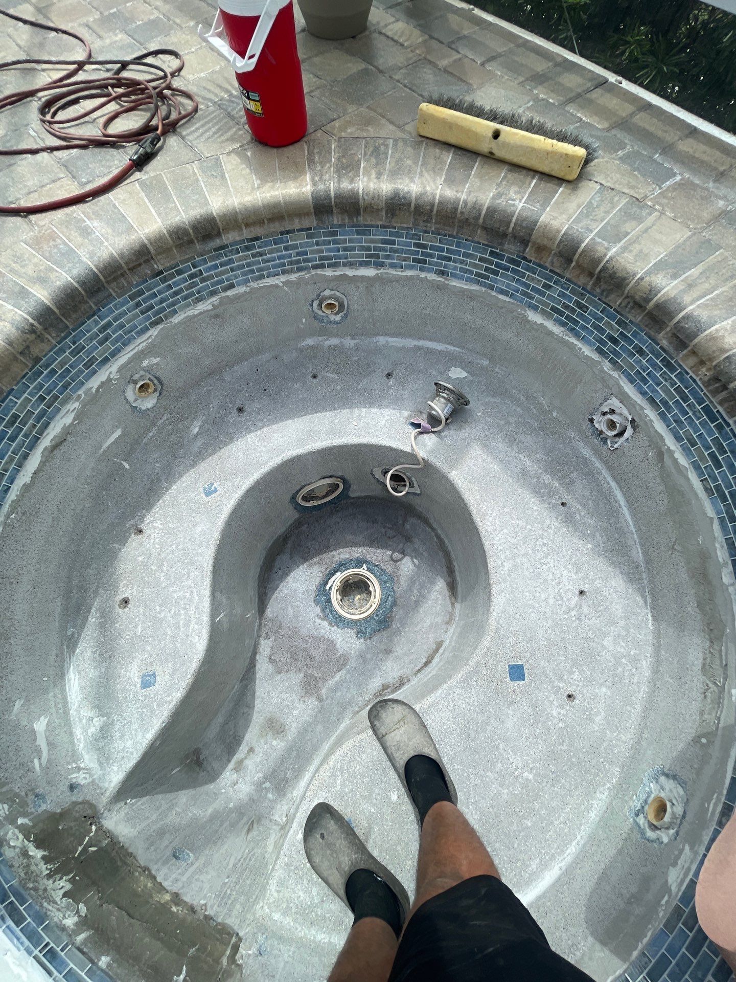 Person standing in a dirty outdoor hot tub or spa, with tools and cords nearby.