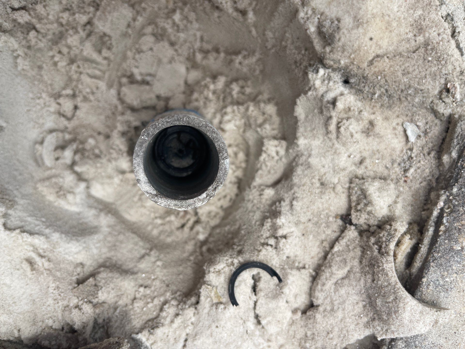 Close-up of a black circular pipe opening set in rough gray concrete.