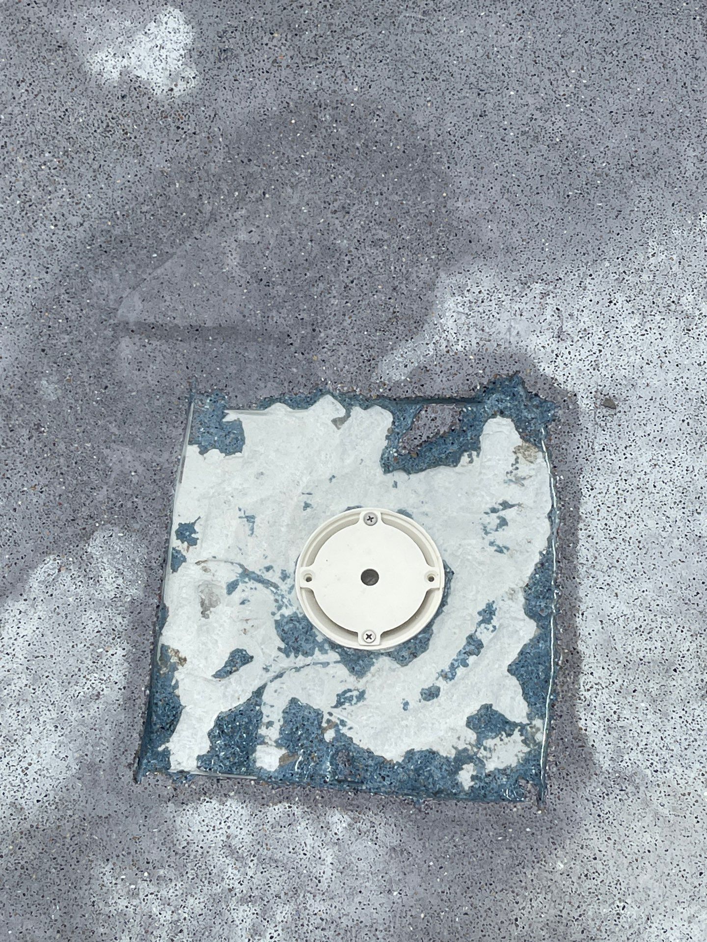 Square concrete patch with a white circular drain cover on gray pavement.