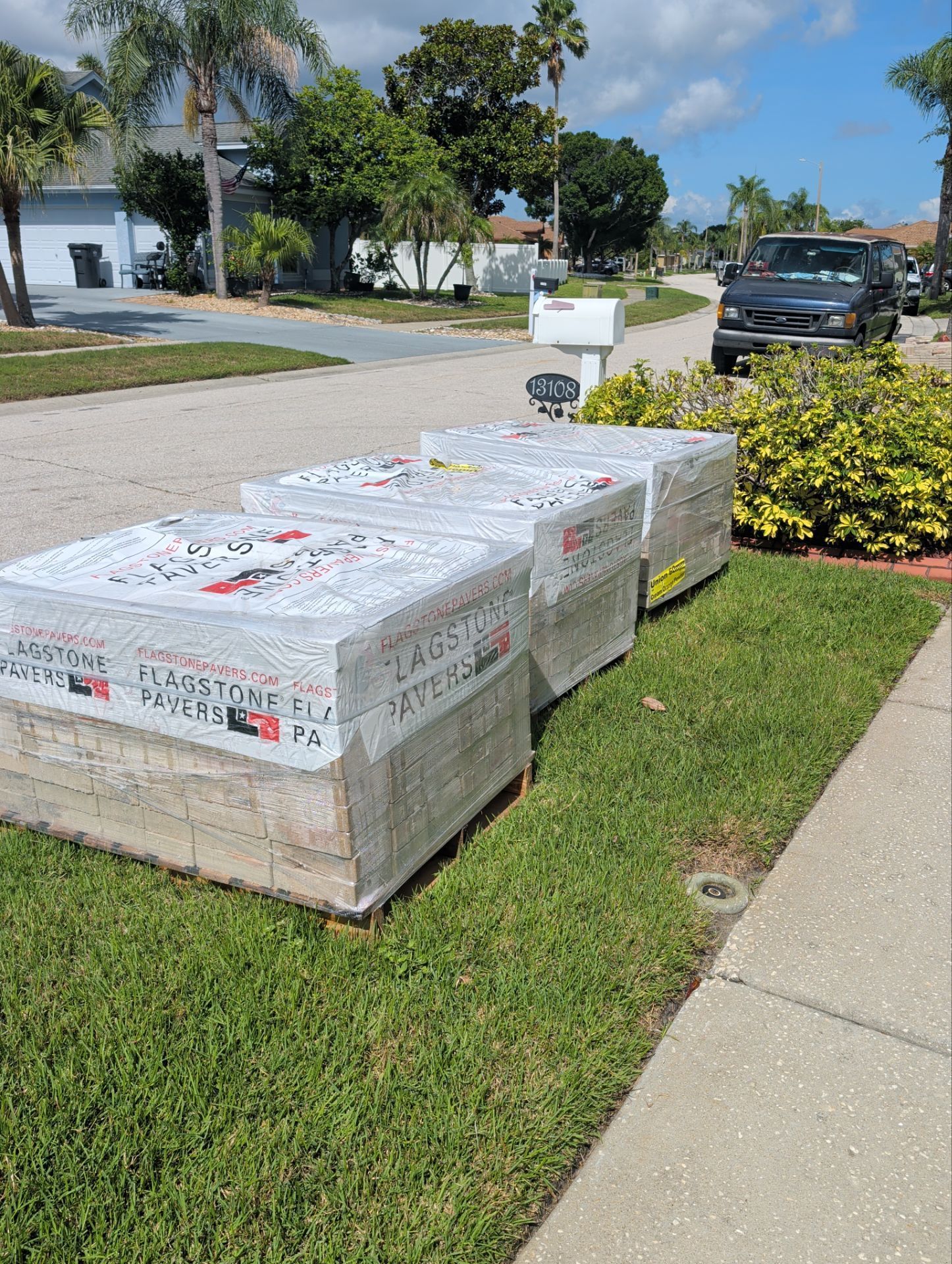 Two wrapped storage crates on a grassy sidewalk beside a suburban street and parked car.