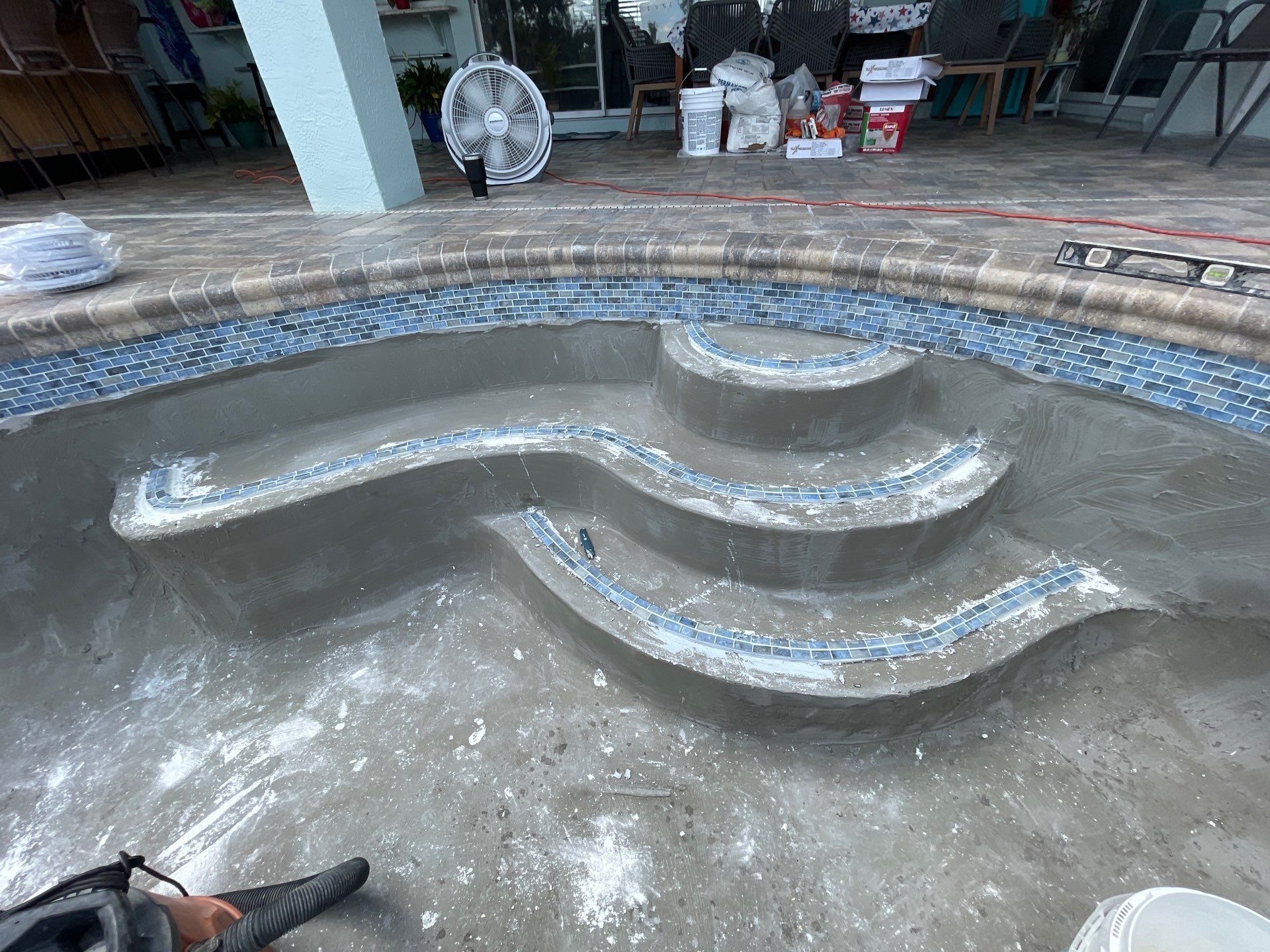 Empty tiled fountain basin with curved blue-tiled steps and shallow water, seen in a courtyard.
