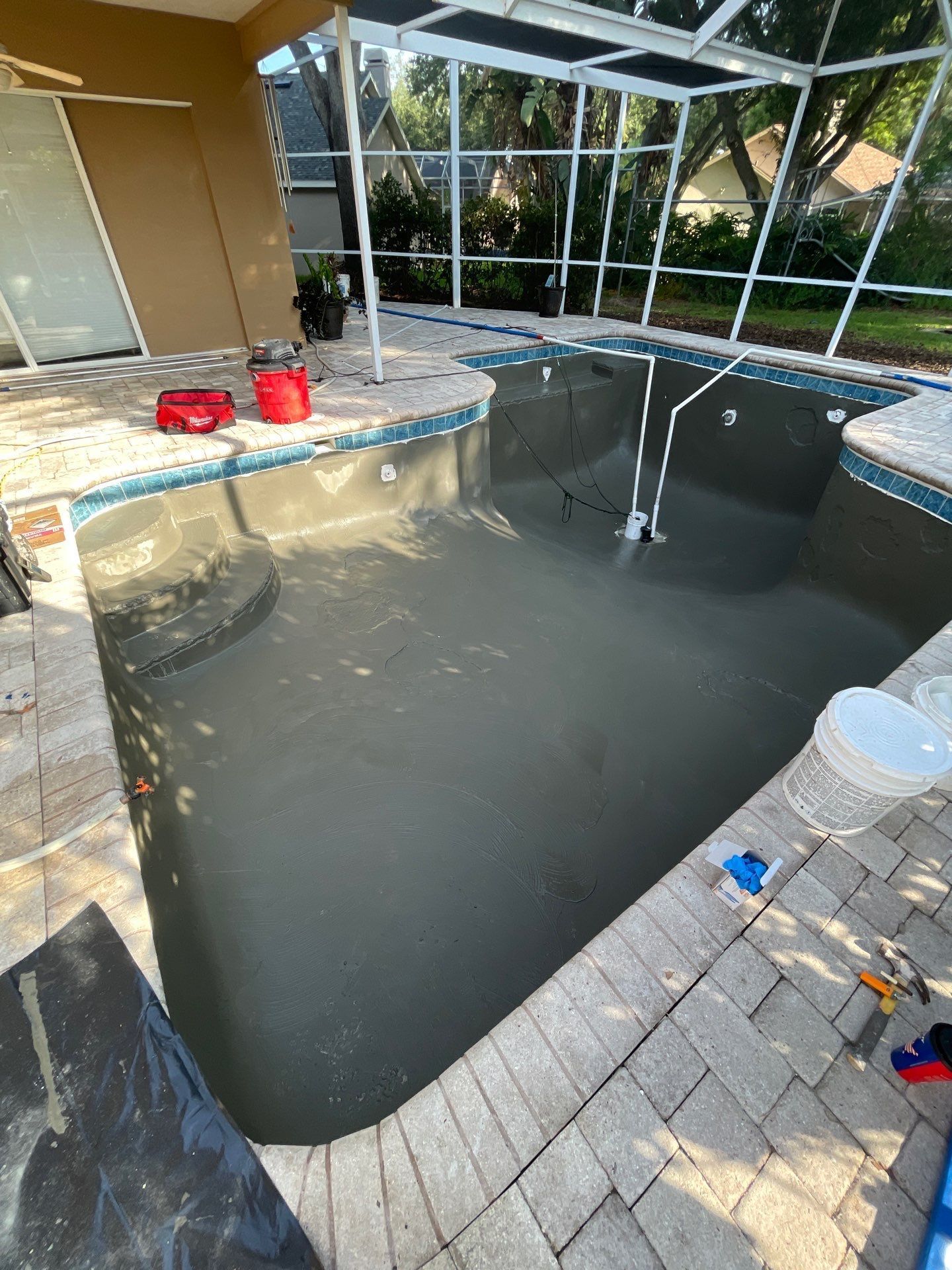 Empty backyard pool under construction with muddy water, pool equipment, and screened enclosure.