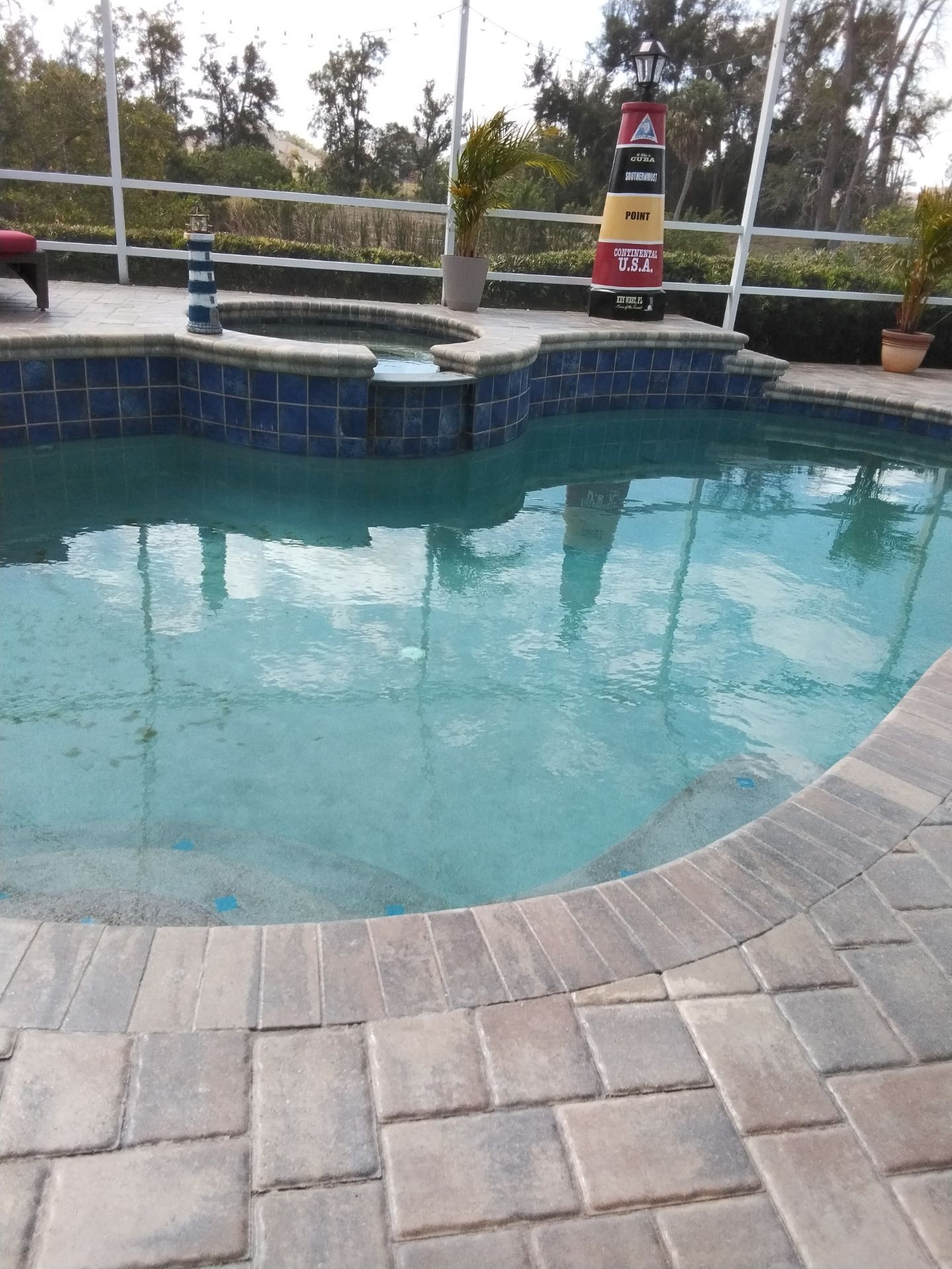 Backyard swimming pool with blue water, stone coping, and a fenced deck with safety signs.