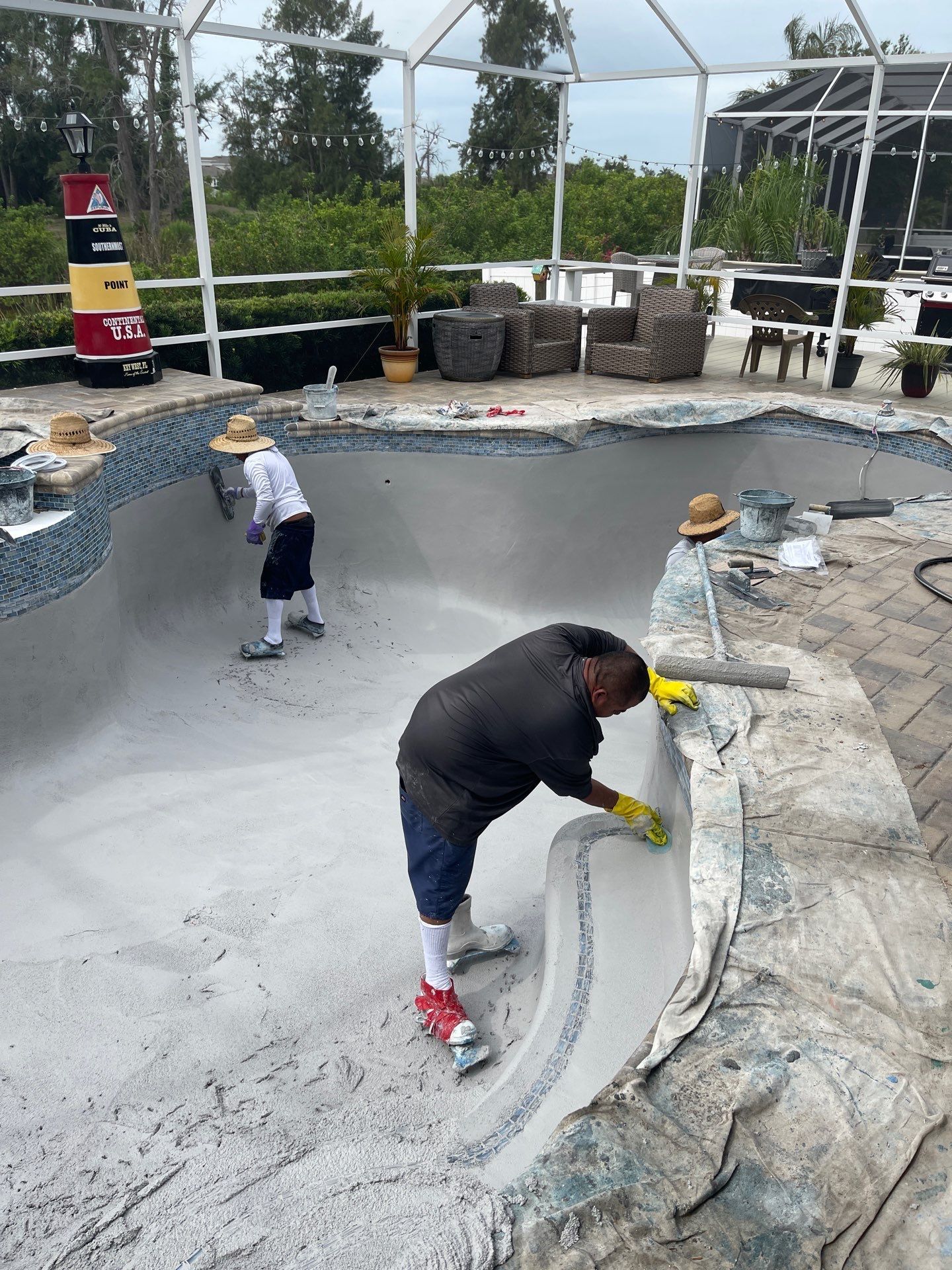 Workers smoothing a concrete pool in a netted outdoor construction area.