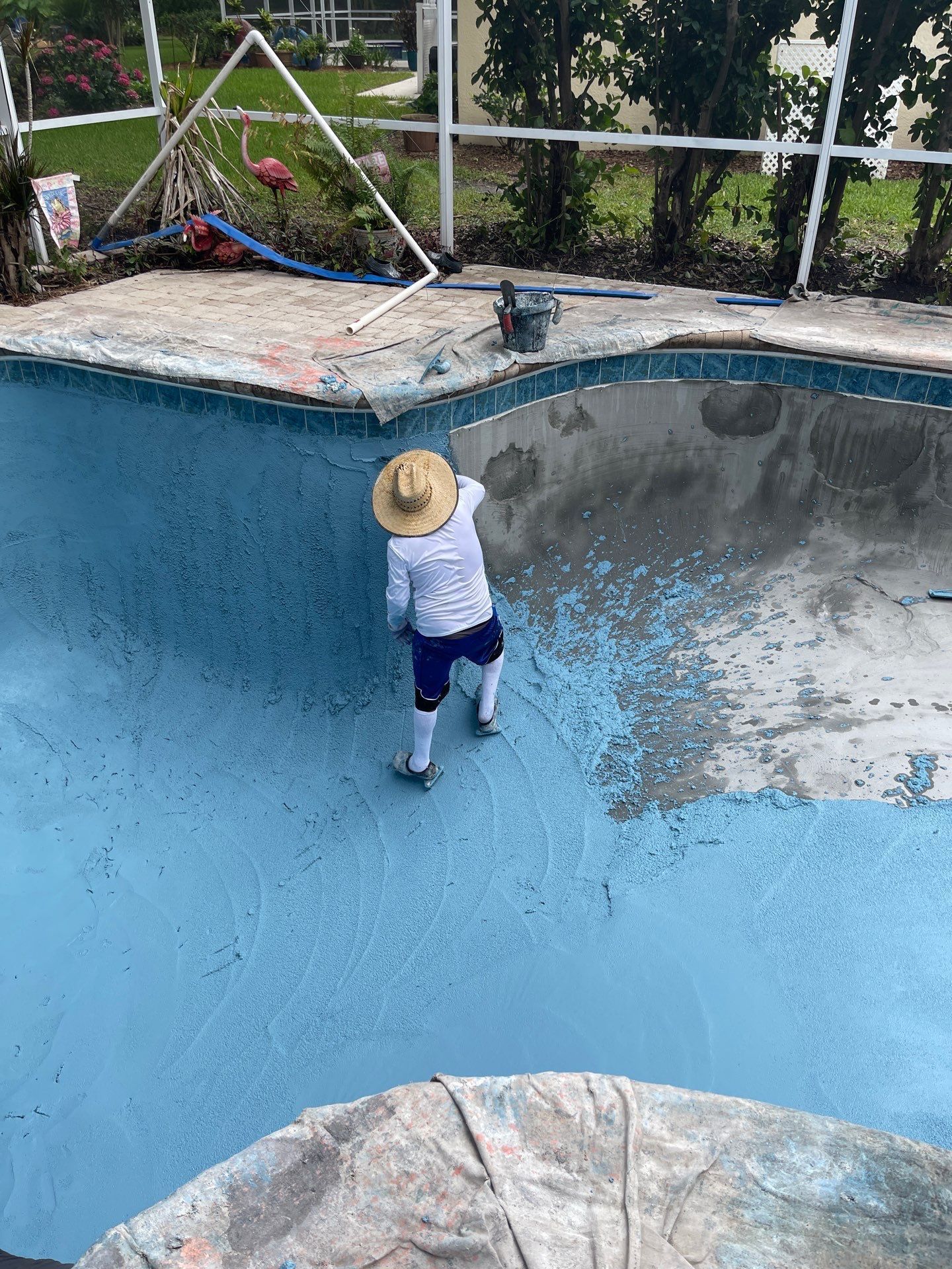 Child in a sun hat standing in an empty blue swimming pool near the shallow end.