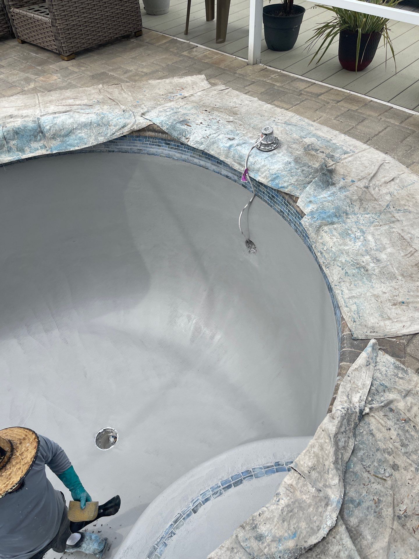 Empty white swimming pool under construction, with stone coping and a worker partly visible at the edge.