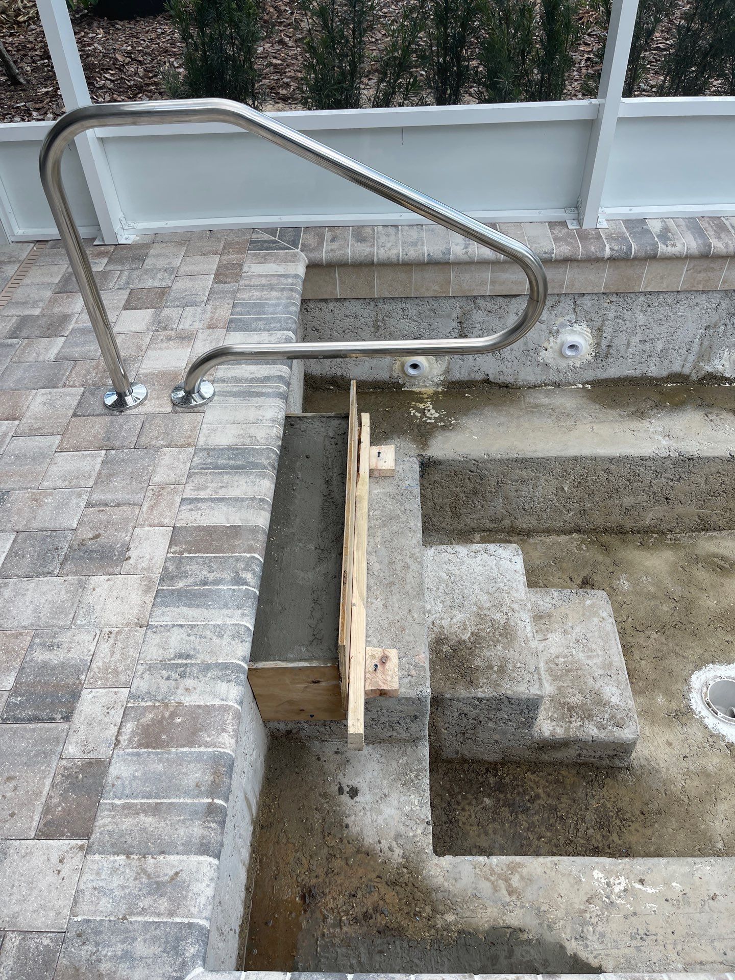 Stainless steel pool handrail beside a tiled pool edge and steps with concrete basin below.
