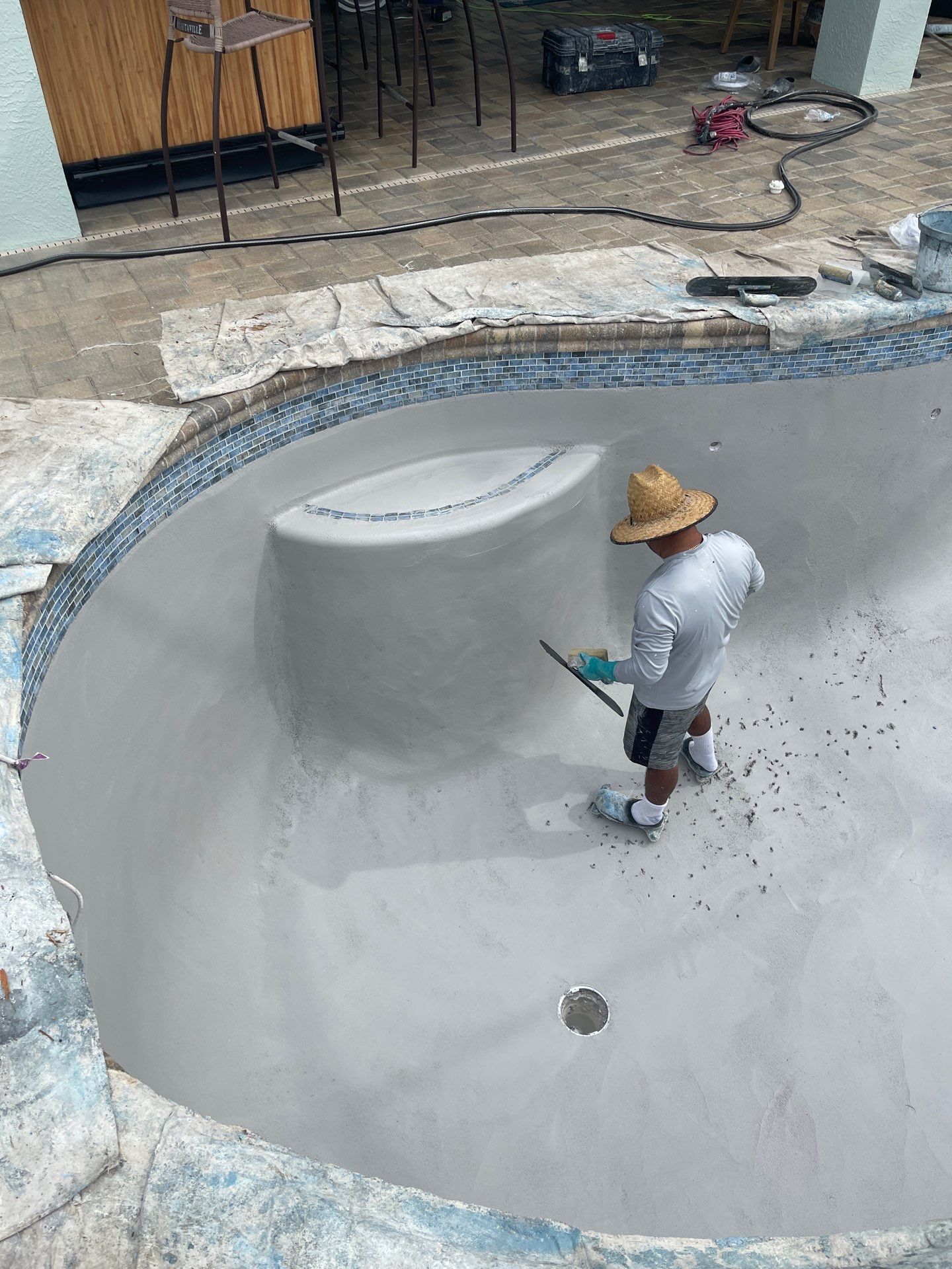 Worker in a straw hat applying coating inside an empty concrete pool.