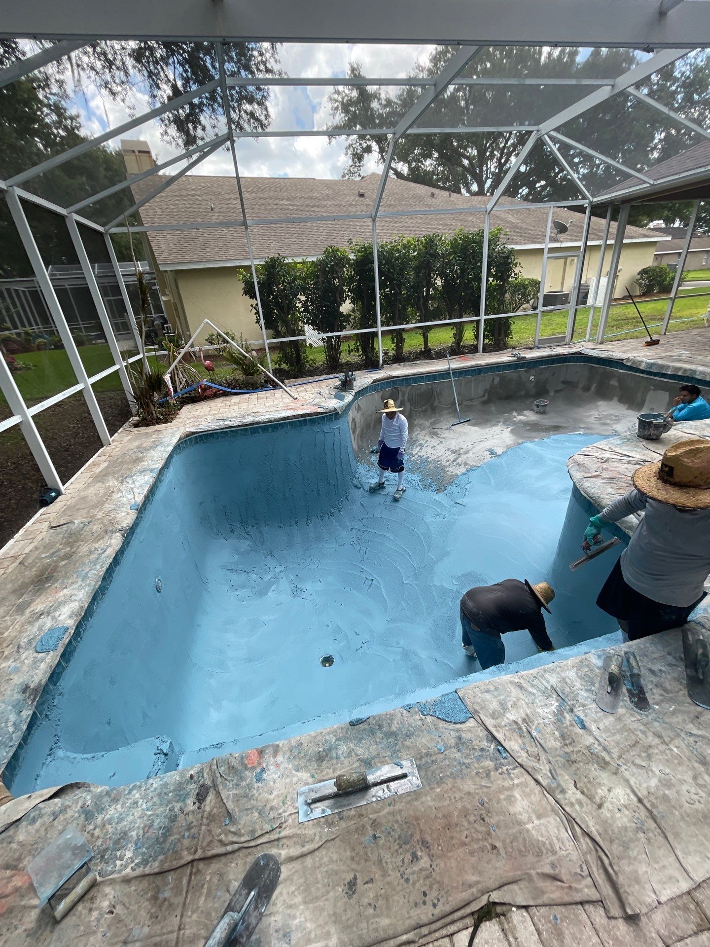 People standing in an empty backyard swimming pool under a screened enclosure, with one person inside.