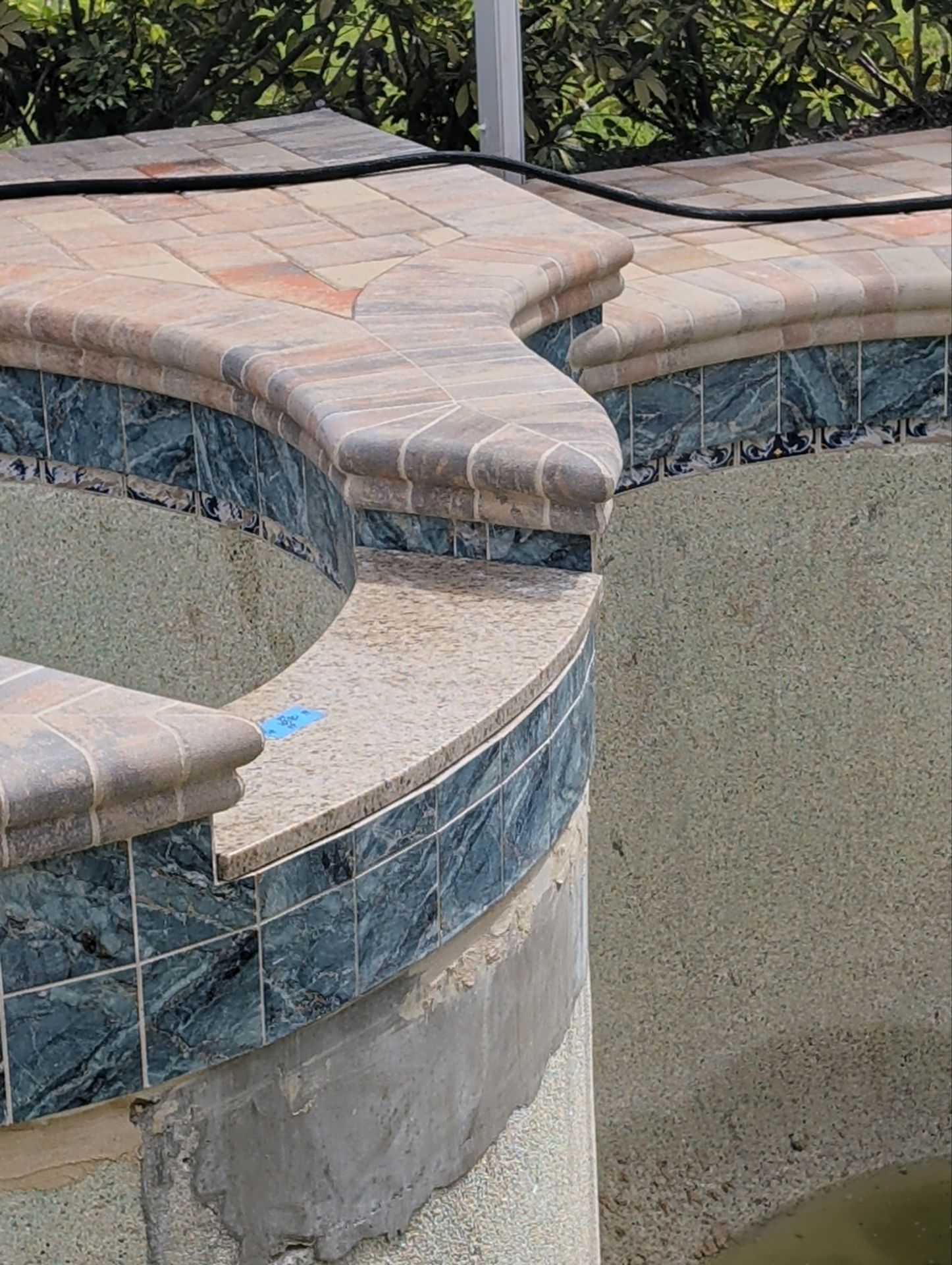Curved tiled spa or pool edge with tan coping and blue accent tiles.
