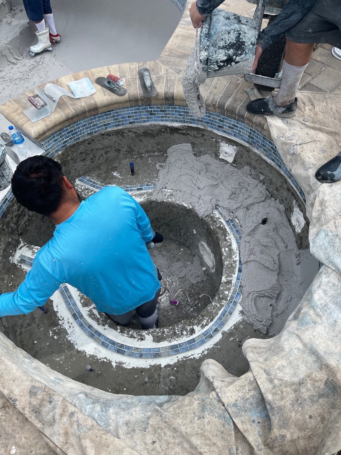 Workers at a concrete well opening, one in a blue shirt inside, others standing around the rim.