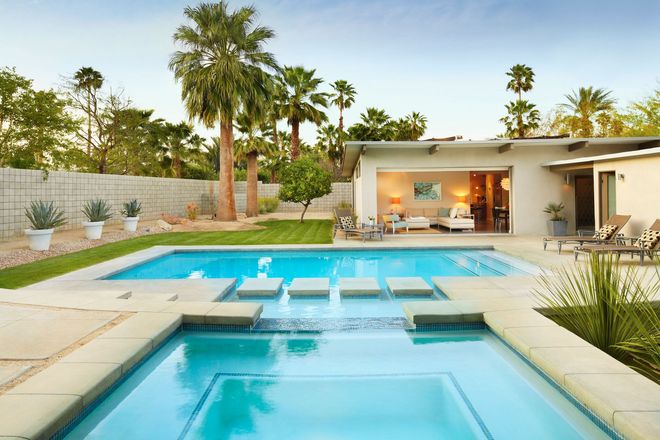 Modern backyard with turquoise pool, spa, palm trees, and a white patio house at sunset