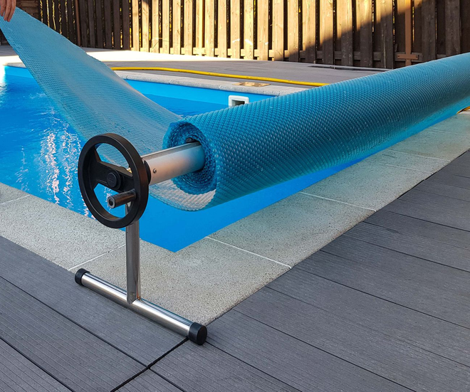 Person adjusting blue pool cover beside a backyard swimming pool