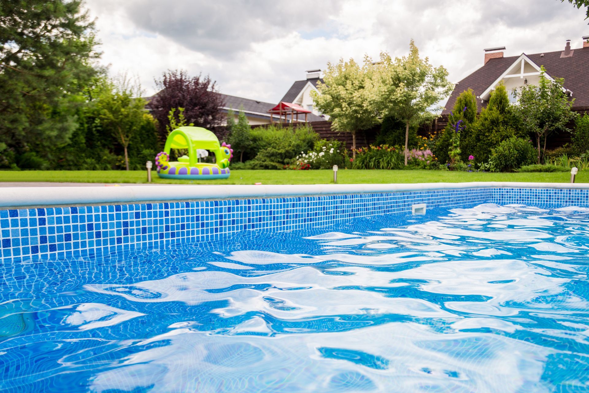 Backyard swimming pool with a green inflatable toy and houses in the background