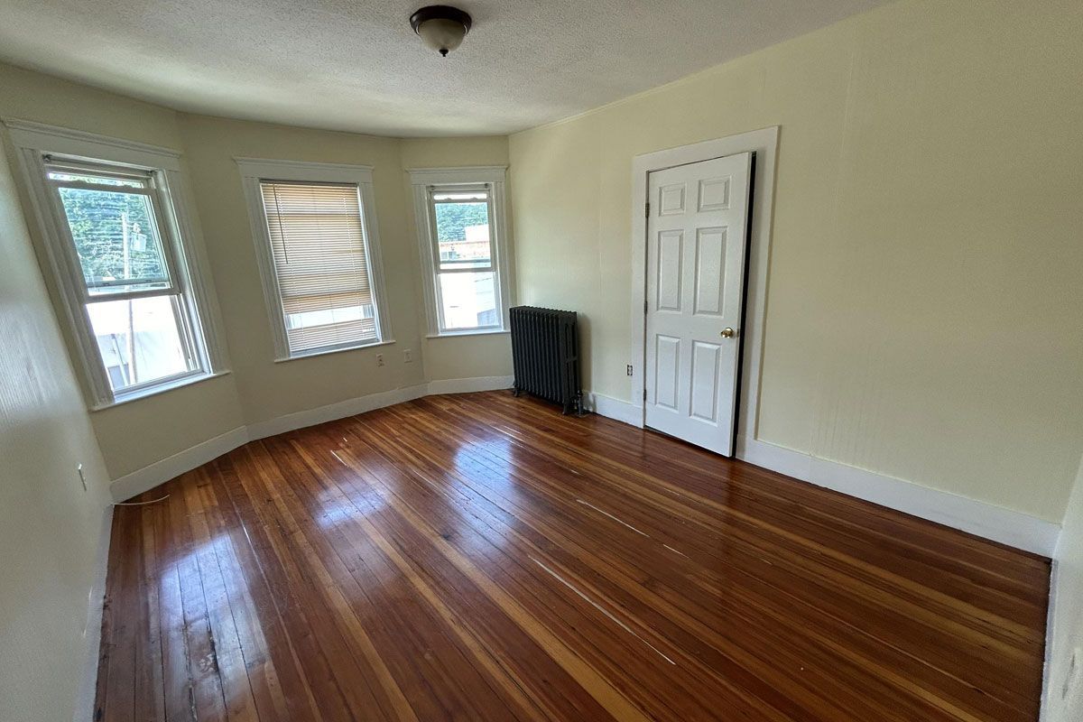 An empty room with hardwood floors and two windows.