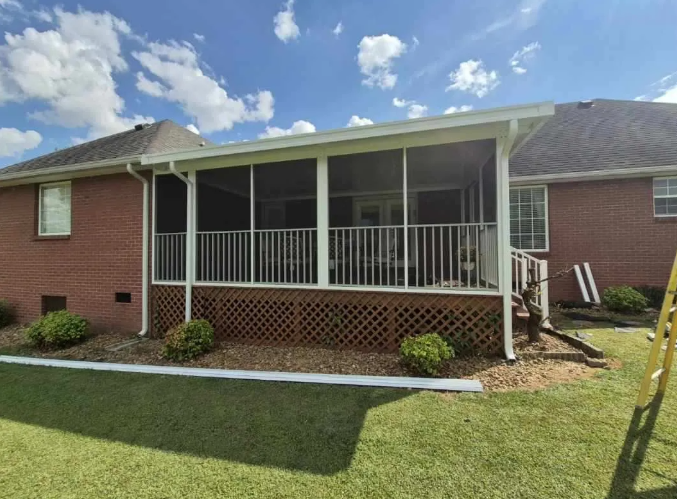 Screened-in porch attached to a brick house with white railings, under a blue sky.