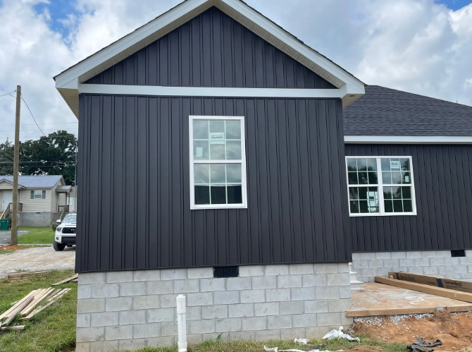 Dark gray vertical siding on a house with white trim and windows on a cinder block foundation.