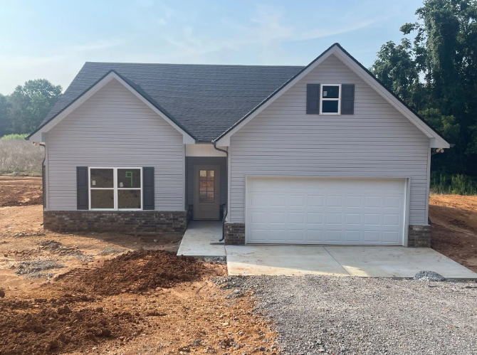 New light gray house with a garage, in a dirt lot, under a blue sky.