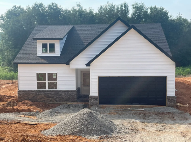 New white house with black roof and garage door, gray stone facade, in construction.