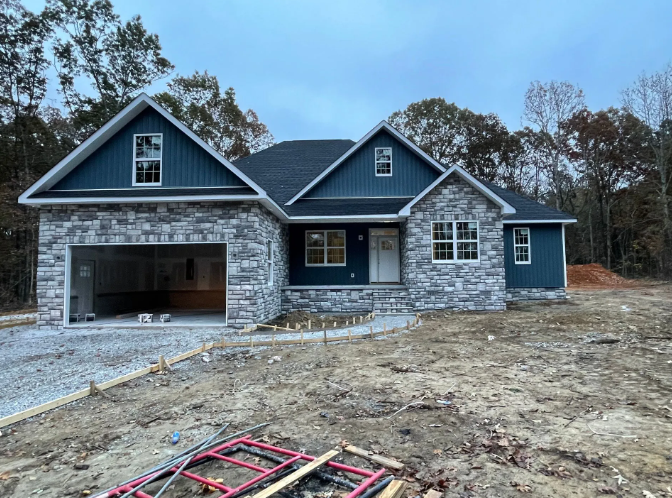 New house exterior with stone facade, blue siding, open garage, cloudy sky.
