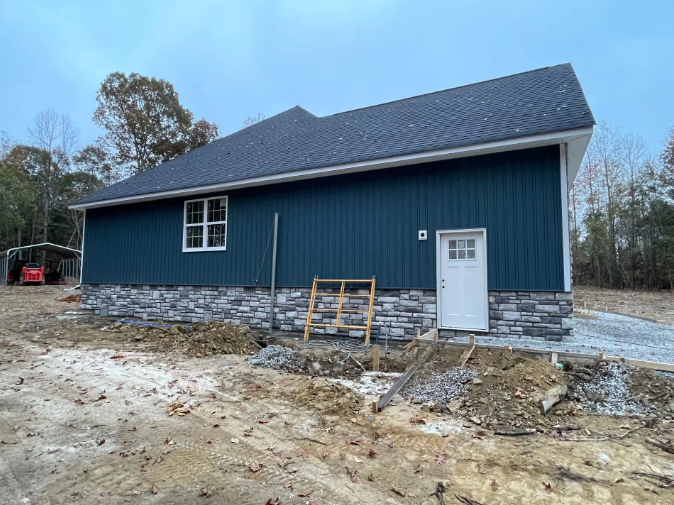 A new house with blue siding, stone foundation, and a white door. Construction debris surrounds the building.