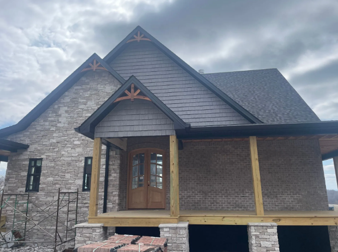 House with gray brick, brown wood accents, and front porch under overcast sky.