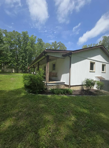 White house with brown trim, porch, and lawn on a sunny day.