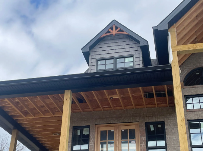 Exterior of a house under construction with gray siding, wooden porch, and black trim.