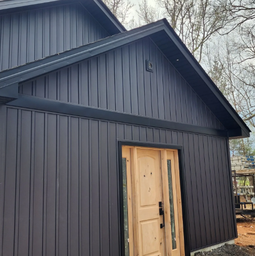 Dark gray house with vertical siding, black trim, and a wooden door.