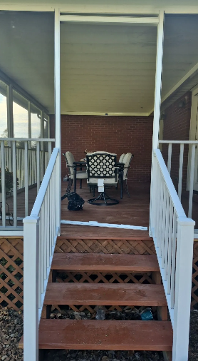 Wooden steps lead to a screened-in porch with a table and chairs.
