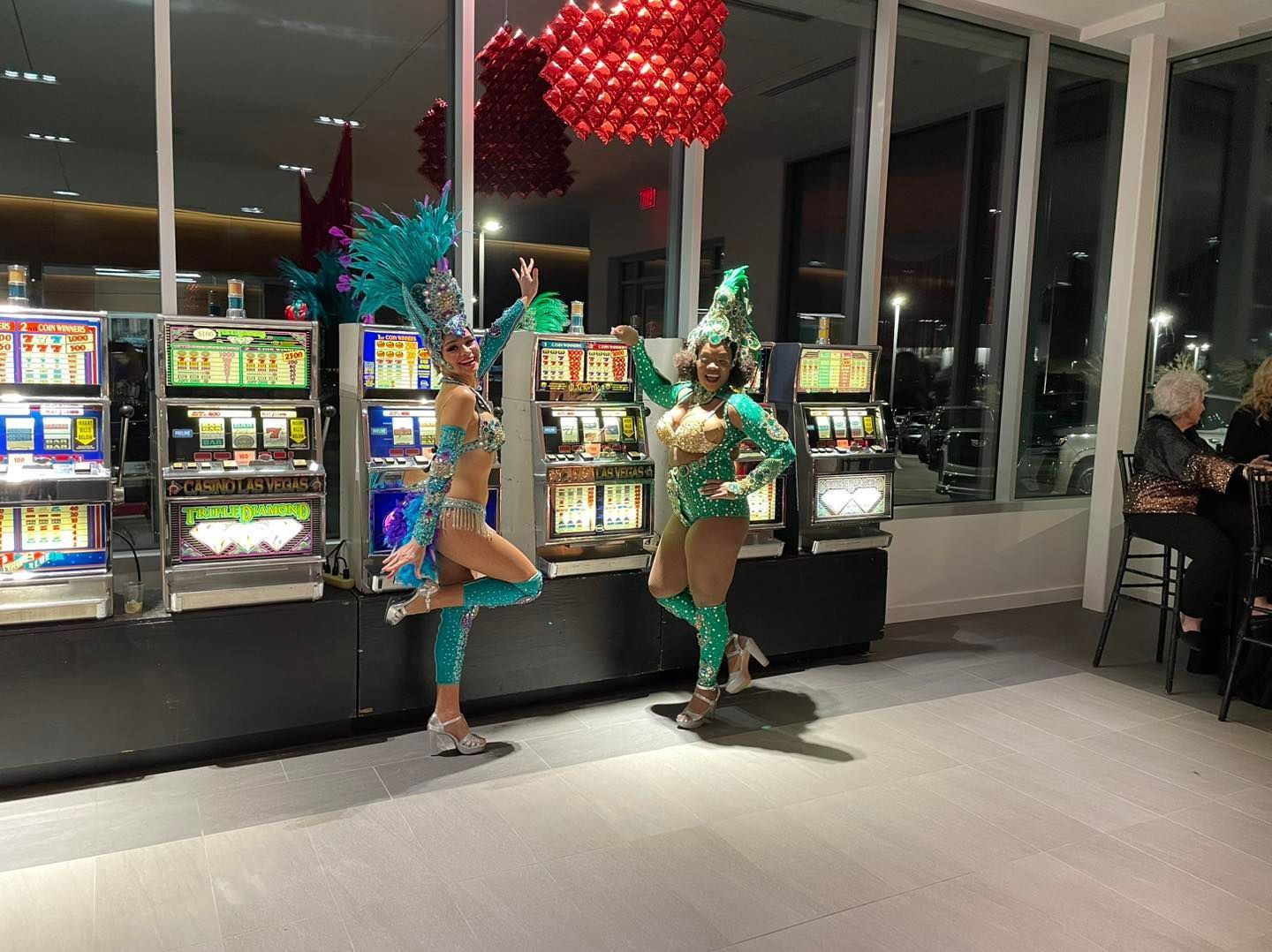 Three women are dancing in front of slot machines in a casino.