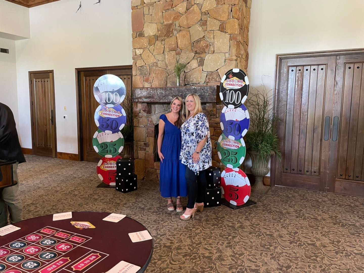 Two women are posing for a picture in front of a roulette table.