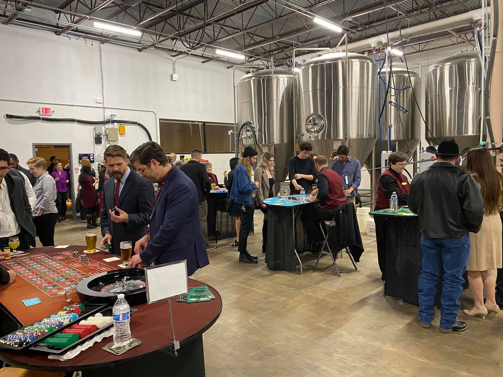 A group of people are standing around tables in a room in a brewery.