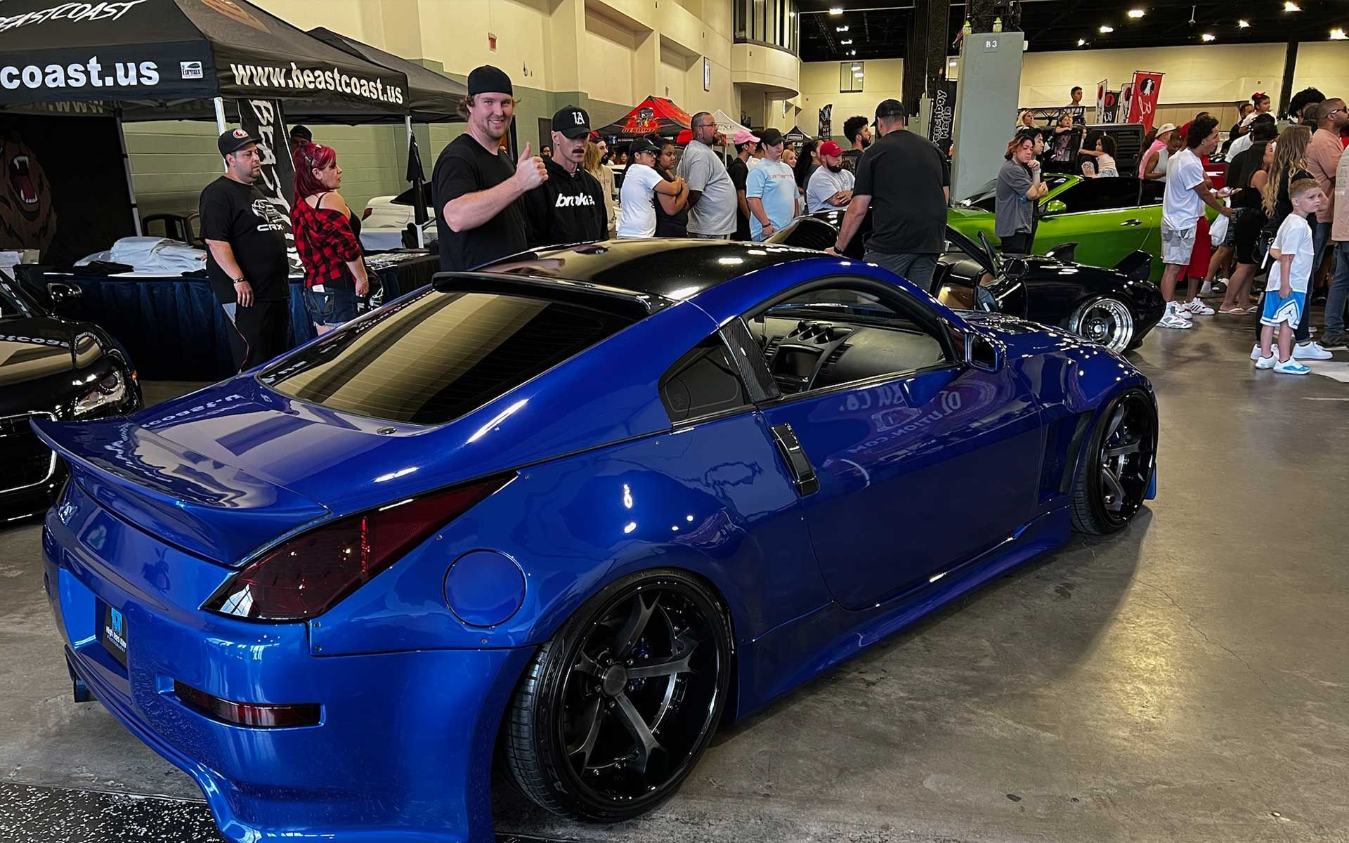 A group of people are standing around a blue car at a car show.