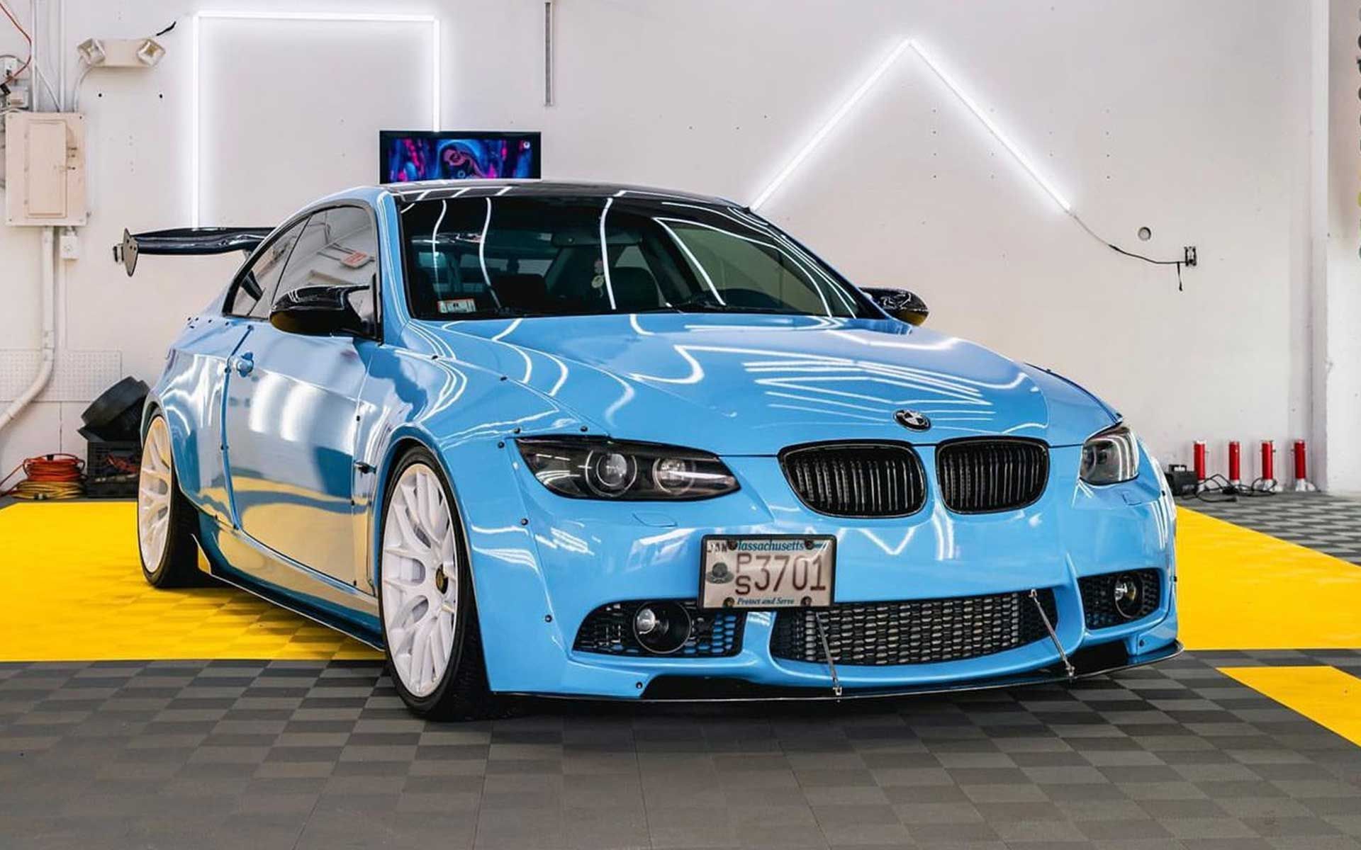 A blue bmw m3 is parked on a yellow mat in a garage.