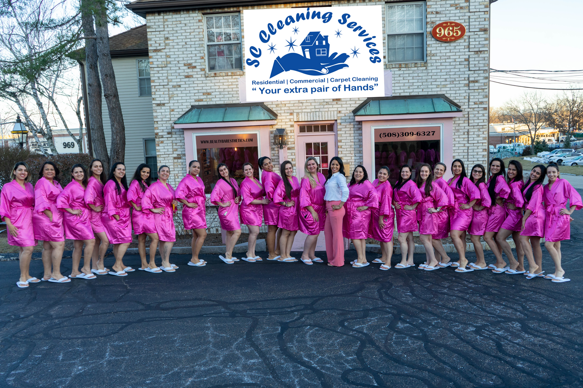 Group of women in pink robes in front of a business with a sign that says