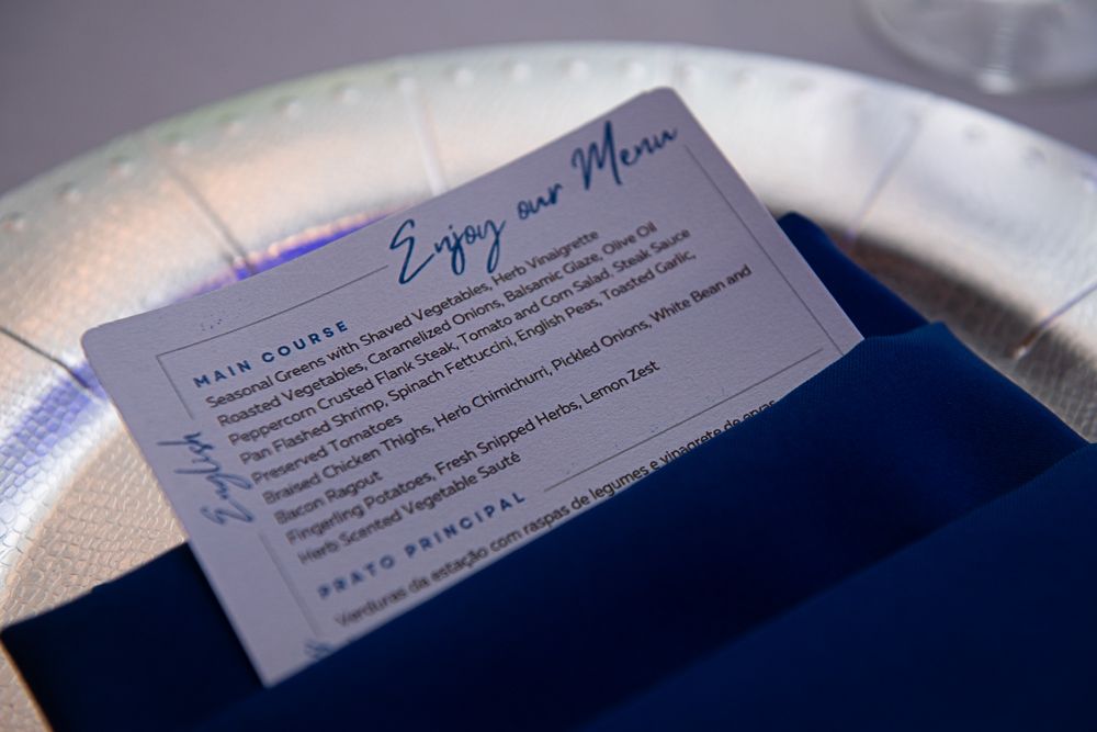 Menu card in a blue napkin on a white plate, listing main courses.