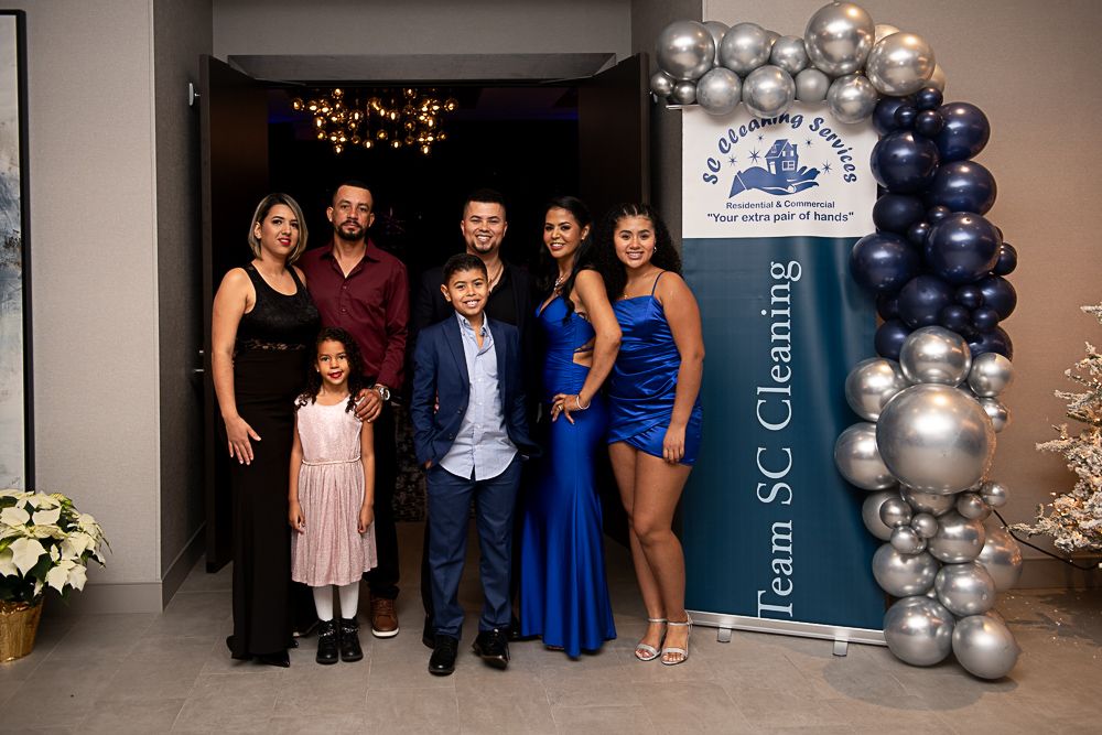 Family poses for photo with a banner. They stand in front of an arch of silver/blue balloons.