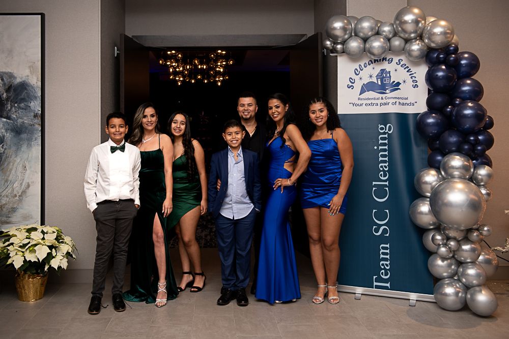 Family poses at an event with balloons and a banner. Formal attire; diverse skin tones; indoors.