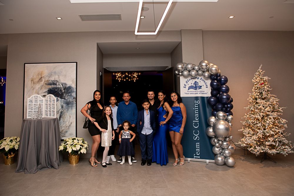 Family poses for a photo at an event with a balloon arch, Christmas tree, and flower arrangements.