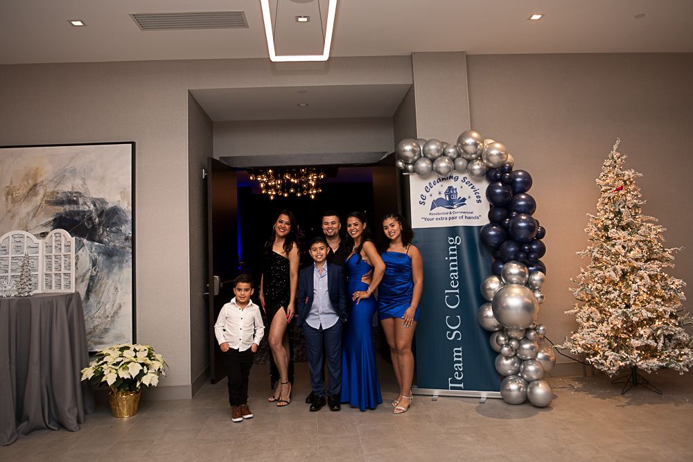 Family posing in front of an entrance decorated with balloons and a Christmas tree, at a formal event.