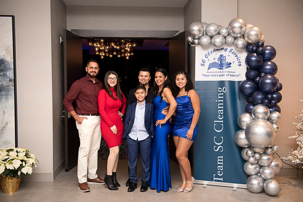 Family poses near a blue banner and balloon arch, celebrating an event.