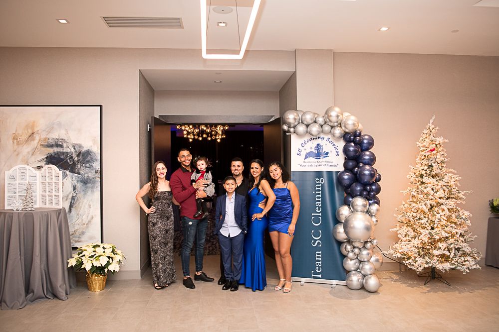 Family poses for a photo at an event, standing in front of an arch of balloons and a Christmas tree.