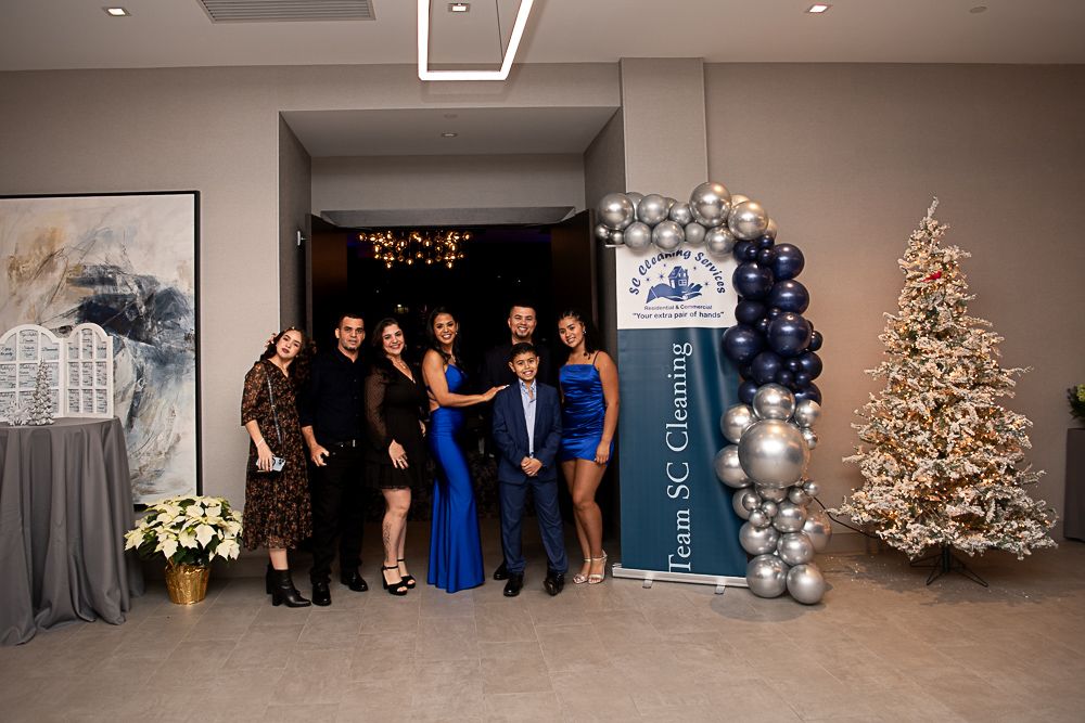 Group of people posing near a banner with balloons and a Christmas tree.