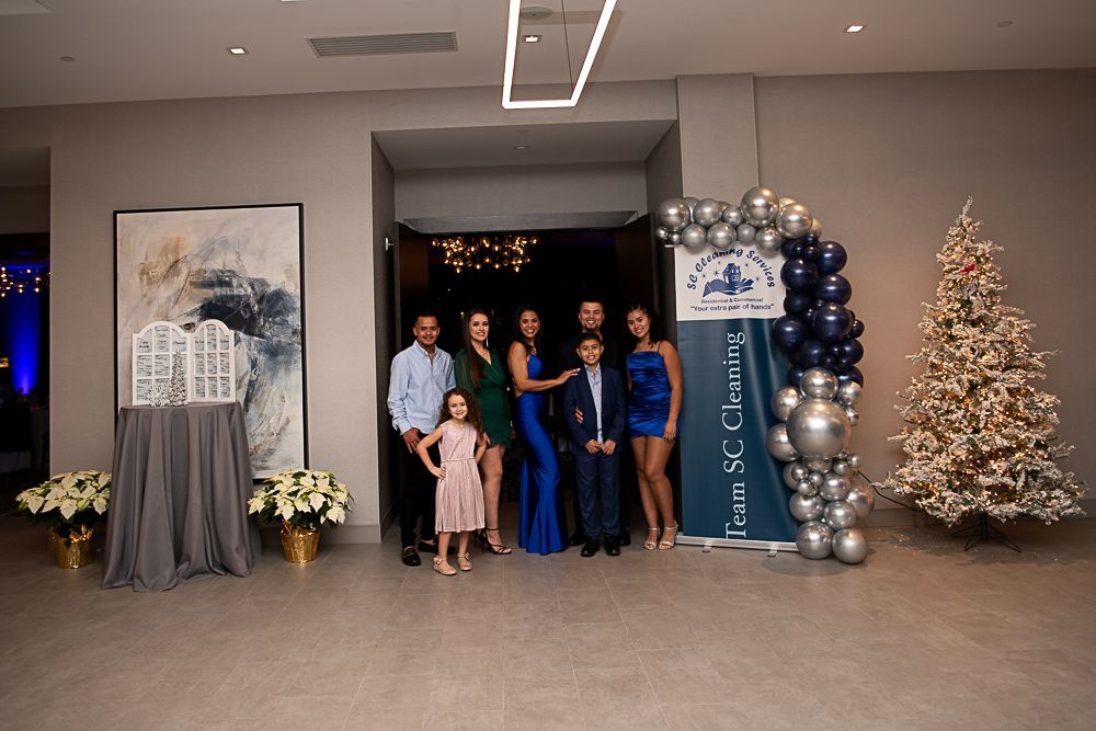 Family posing for a photo at an event, near a balloon arch, banner, and decorated Christmas tree.